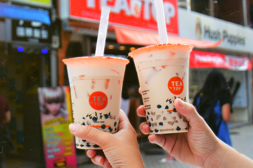 Bubble Tea and Boba Tea from Tea Top Shop: “Two hands holding cups of bubble tea and boba tea from Tea Top shop, emphasizing the vibrant street culture and popularity of bubble tea in urban settings.”