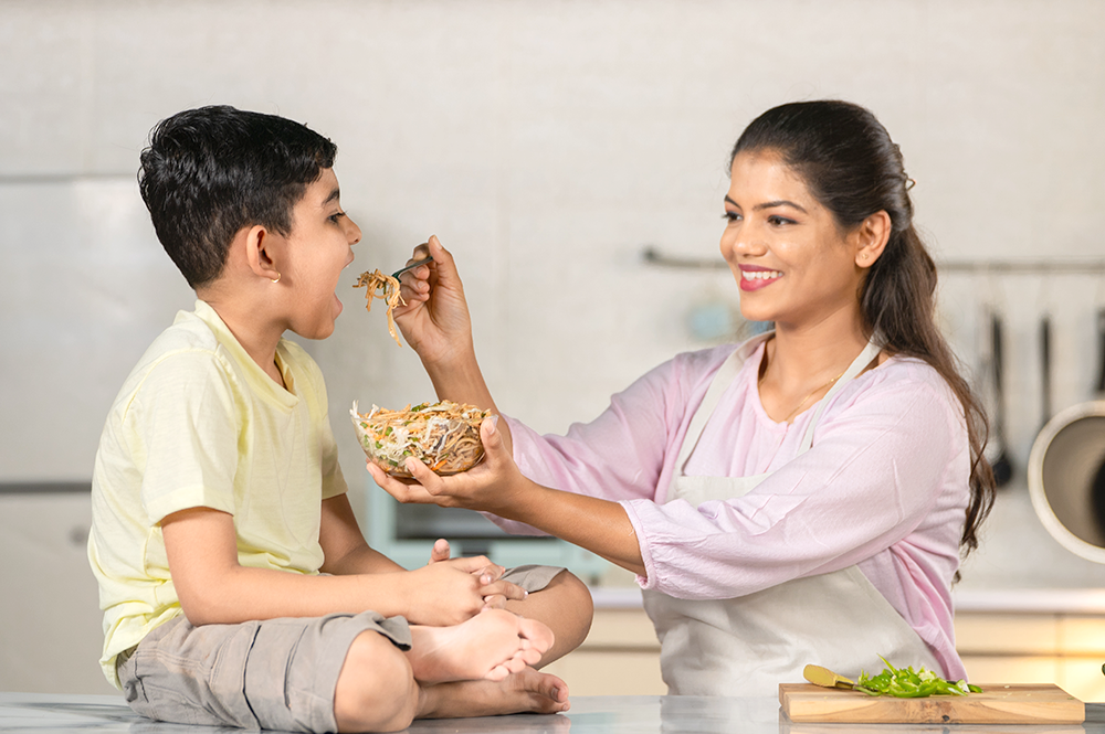 A smiling woman feeding healthy food to a child, highlighting the importance of clean eating habits from a young age