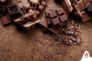 CHOCOLATES AGAINST A BROW BACKGROUND WITH COCOA AND COCOA SEEDS STREWN ABOUT. COCOA REPLACERS