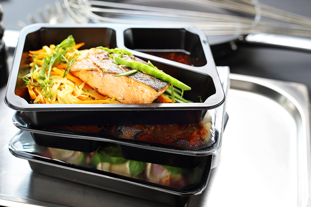 A ready-made meal of fish, vegetables and noodles in a partitioned black plastic container, exemplifying convenience foods.